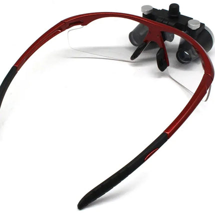 Red and black surgeon's magnifying glasses with a clear protective lens and black temple tips, shown on a white background.