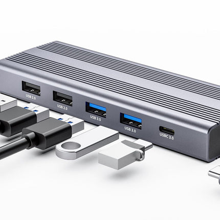 A silver aluminum USB-C hub with multiple ports, shown with various USB-C and USB-A cables on a clean white background.