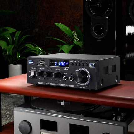 Audio amplifier on a wooden table with speakers and plants in the background
