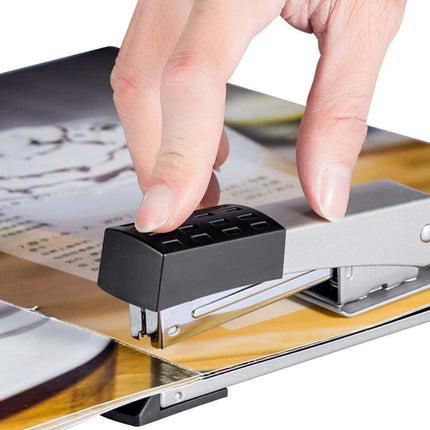 Hand using a small black and silver device on a wooden surface with a magazine underneath.