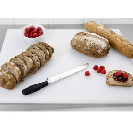 Loaves of bread, a knife, and raspberries on a white cutting board.