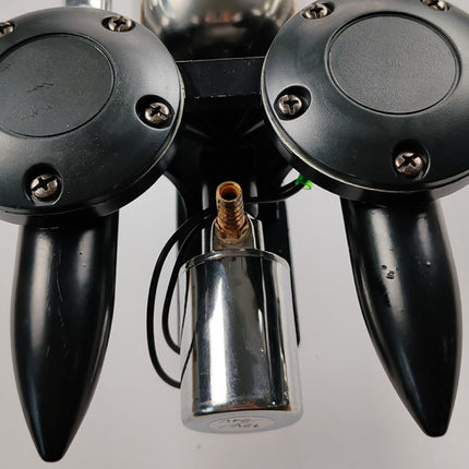 Close-up of a black dual-grip controller or robotic hand component with two large circular black pads, pointed black fingers, and a shiny silver cylindrical part in the center against a light gray background.