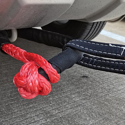 Red rope tied in a knot with a black strap attached to a vehicle's undercarriage.