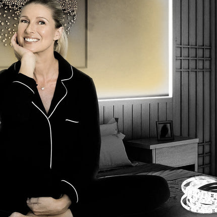 Woman in black pajamas sitting on a bed with LED strip lights in the foreground.