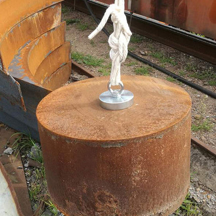 Rust-colored cylindrical object with a white rope and metal hook on a railway track background