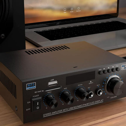 Black audio amplifier on a wooden surface with a laptop in the background