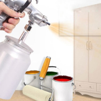 Person using a spray paint gun with paint cans and a white cabinet in the background