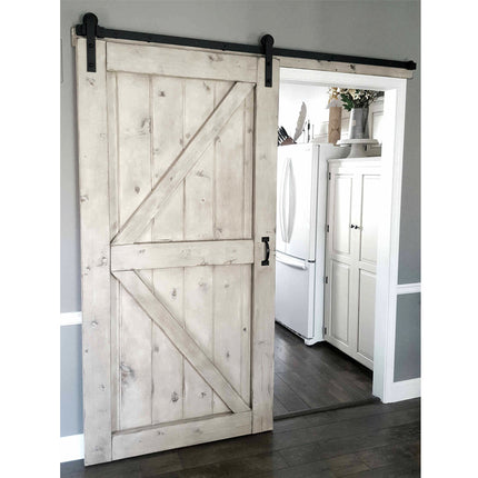 A rustic white-washed wooden sliding barn door with a black metal rail and hardware, shown partially open in a doorway leading to a kitchen.