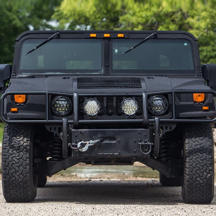 Black military-style vehicle with large tires on a gravel surface.