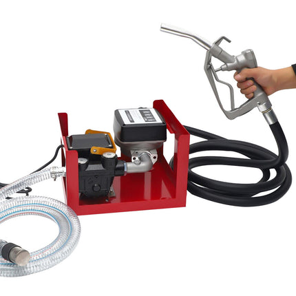 A red portable fuel pump kit with a black hose, clear transfer hose, digital display, and a hand holding a gray fuel nozzle on a white background.