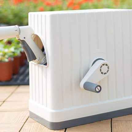 White hose reel with a spray gun on a wooden surface with plants in the background