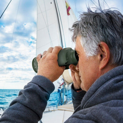 Man on a sailboat using binoculars to look out at the water