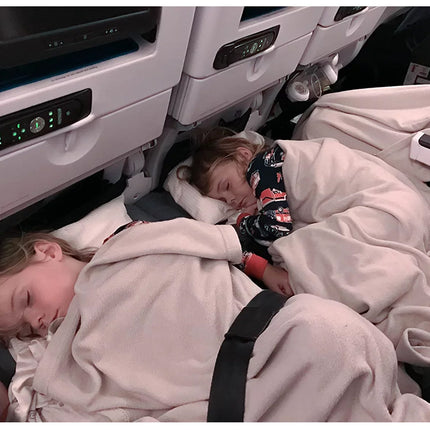 Two children sleeping in airplane seats with blankets and seat belts.
