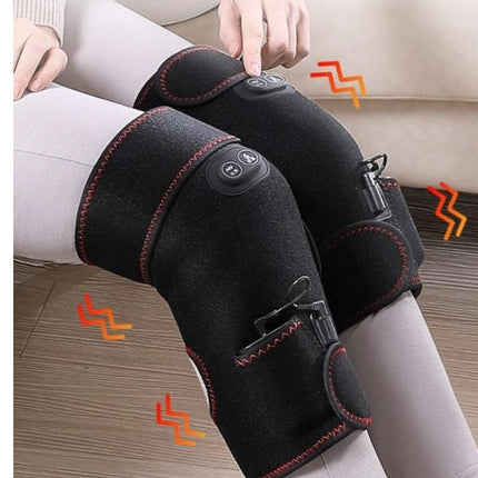Person wearing black knee support with heating elements on a wooden floor.