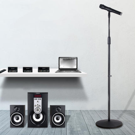 Microphone stand in a room with audio equipment and a laptop on a shelf.