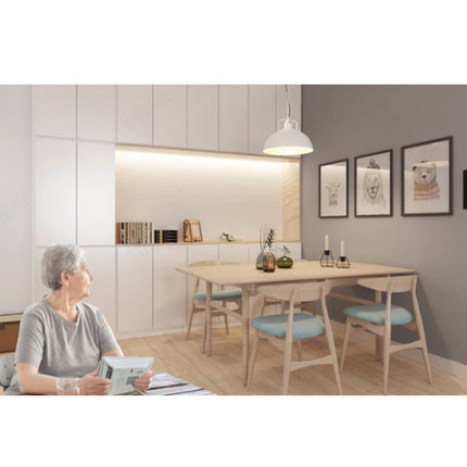 A woman sits at a dining table in a modern, minimalist dining room with light wood furniture, a gray accent wall with framed art, and built-in cabinetry in the background.