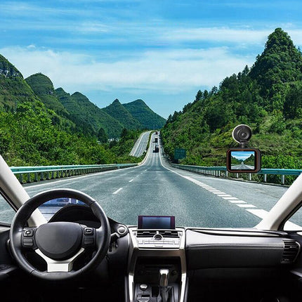 Car dashboard view with a rearview camera and monitor on a scenic road.