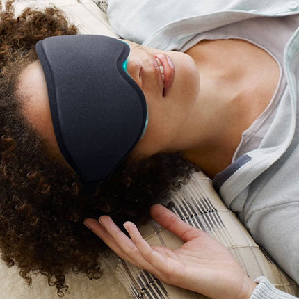 Person wearing a black sleep mask lying on a bed.