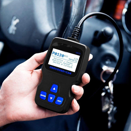 A hand holding a black OBD2 scanner diagnostic tool with a blue backlit screen and blue buttons, connected to a car's ignition system in a dark car interior.