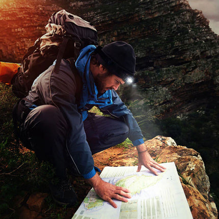 Person on a mountain using a map with a headlamp