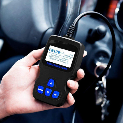 A hand holding a black OBD2 scanner diagnostic tool with a screen and blue buttons, connected to a car's ignition system inside a vehicle.