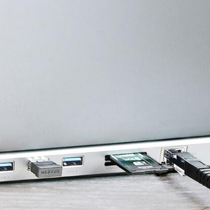 Close-up of the side of a silver laptop showing USB-A and USB-C ports, with a SIM card ejected from one port and a black Ethernet cable plugged into another, resting on a light wood surface.