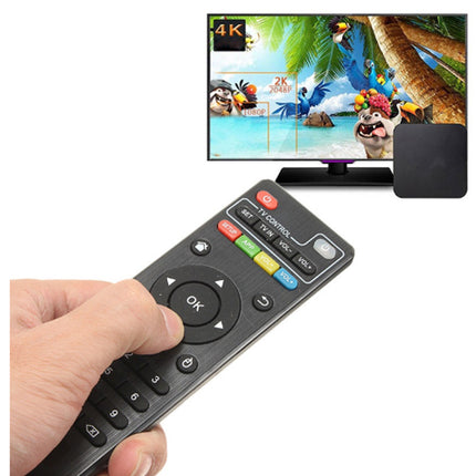 A hand holding a black remote control in front of a small TV and a black streaming box on a white background. The TV displays colorful cartoon characters and tropical scenery.