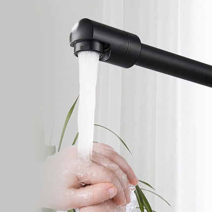 A matte black wall-mounted kitchen faucet with water running from the spout, shown with a hand washing beneath it against a light neutral background.