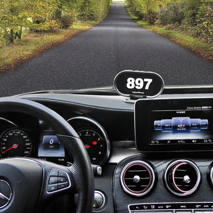 Car dashboard with a navigation device displaying '897' on a road surrounded by trees.