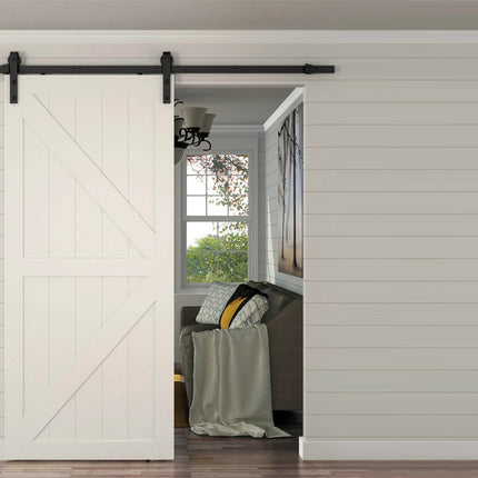 A white shiplap barn-style sliding door with a black metal rail, shown installed in a bright room with wood flooring and a glimpse into an adjacent living space.