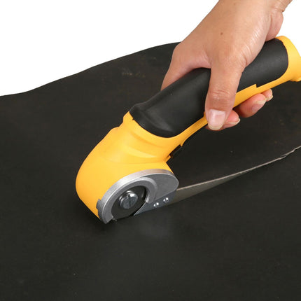 A rotary cutter with a yellow and black handle being held by a hand over a black sheet of material, isolated on a white background.
