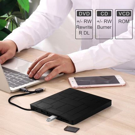 A black portable external optical drive connected to a laptop on a light wood desk, with a smartphone nearby and a small SD card. A person in a white shirt is partially visible at the top, and feature callouts for DVD, CD, and VCD appear in the upper right.