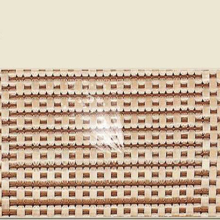 A close-up of a woven mat or placemat with a tight basketweave pattern in natural tan and brown tones, shown against a light beige background with small green leaf accents in the top corners.