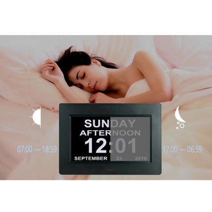 Digital clock display with time and date on a blurred background of a person lying down.