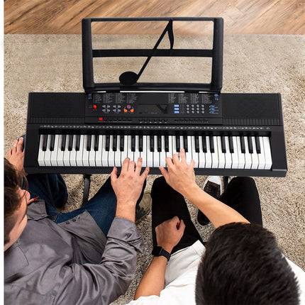 Two people playing a keyboard on a carpeted floor.