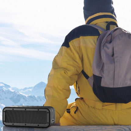 Person in yellow snowsuit with backpack sitting on a snowy mountain, holding a black portable speaker.