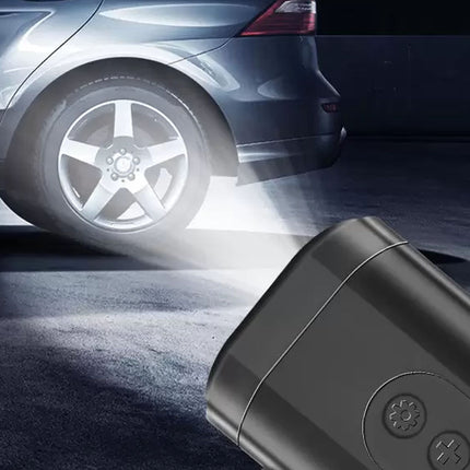 A close-up of a black cylindrical device in the foreground with a bright beam of light shining toward a car wheel in a dark outdoor setting. The device appears to be a portable light or projector accessory.