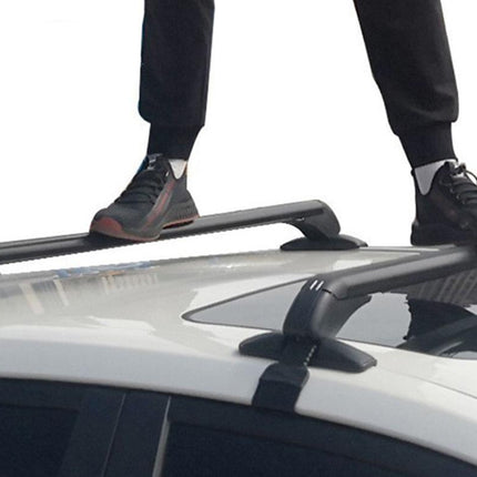 Black roof rack crossbars mounted on a white car roof, with a person's legs and shoes visible standing on top of the vehicle.