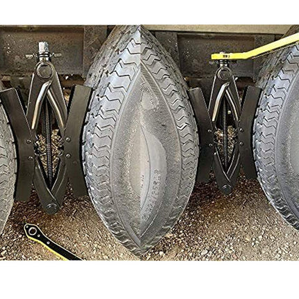 A close-up of a heavy-duty tire jack supporting a large vehicle tire, with a second jack visible beside it on a gravel surface.