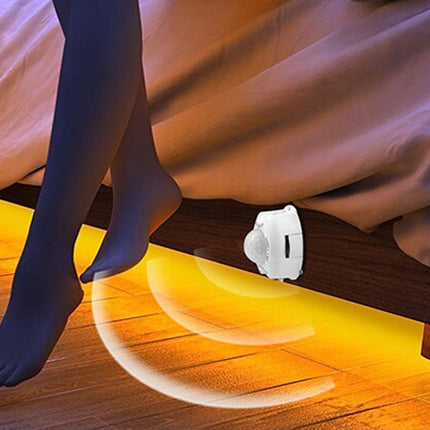 Person wearing black tights with a glowing floor light on a wooden floor.