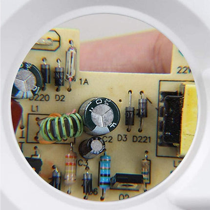A close-up view of a circuit board with electronic components visible through a circular magnifying lens, with a finger pointing at one of the components.