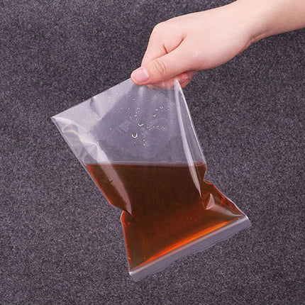 Hand holding a clear plastic bag with brown liquid against a dark gray background