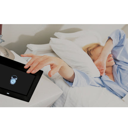 Person in bed using a tablet with an alarm clock app displayed.