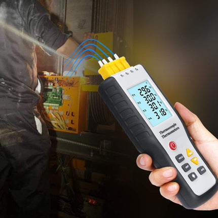 A hand holding a handheld thermal imaging thermometer with a yellow and black body, displaying a digital temperature reading, with a blurred background of a person working in a workshop.