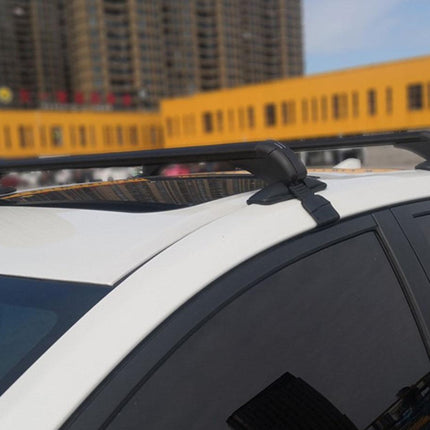 Black roof rack crossbars mounted on the roof of a white car, shown in an outdoor setting with blurred buildings in the background.