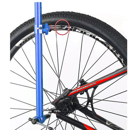 Close-up of a bicycle wheel and rear hub with a blue vertical tool inserted near the wheel, on a white background.