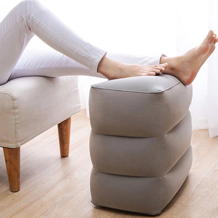 Person sitting on a chair with feet propped up on a cushioned ottoman in a room.