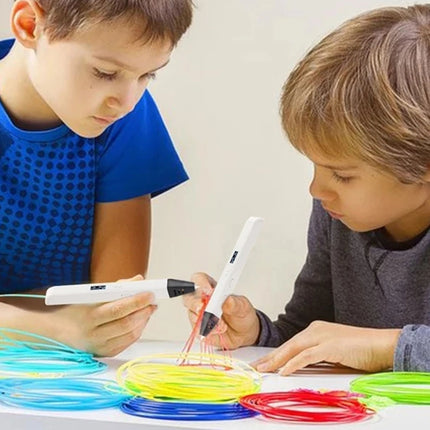 Two boys sitting at a table using white 3D printing pens to create colorful plastic structures, with stacks of blue, yellow, red, and green filament coils on the table.
