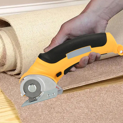 A person's hand holding a yellow and black utility knife cutter as it slices through a roll of tan carpet or flooring over a wood floor.