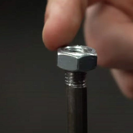 A close-up of a hand holding a silver hexagonal bolt against a dark background.